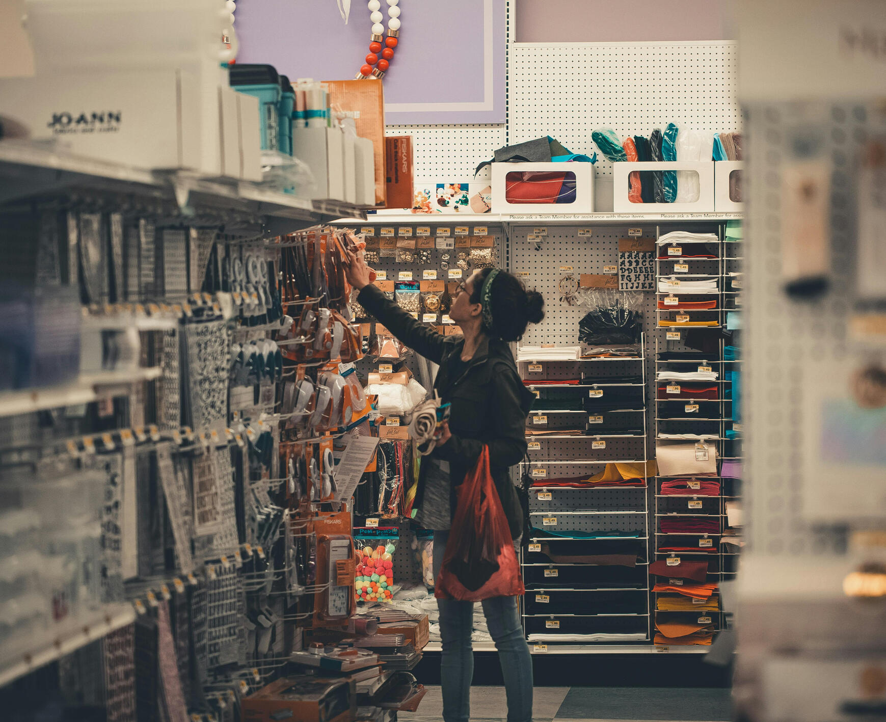 Our Mission Image An image displaying a woman choosing a tool in an aisle She is surrounded by aisles of tools and other things that she might beneficial for her project.